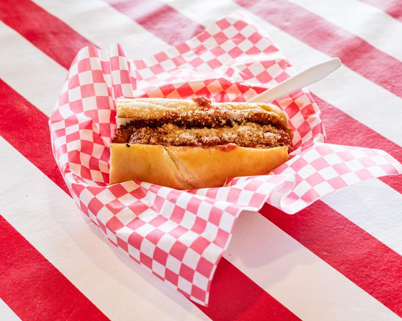 Meatball sub with red sauce and parmesan cheese, served in checkered paper on a striped table.
