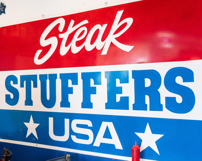 Red, white, and blue sign for "Steak Stuffers USA" with a red ketchup bottle below.