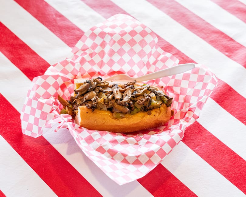 Cheesesteak sandwich with mushrooms, onions, and peppers in a red and white checkered basket.