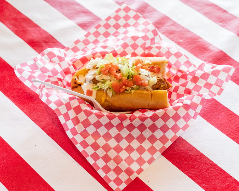 A fried chicken po'boy sandwich with lettuce, tomatoes, and sauce in a red and white checkered wrapper.