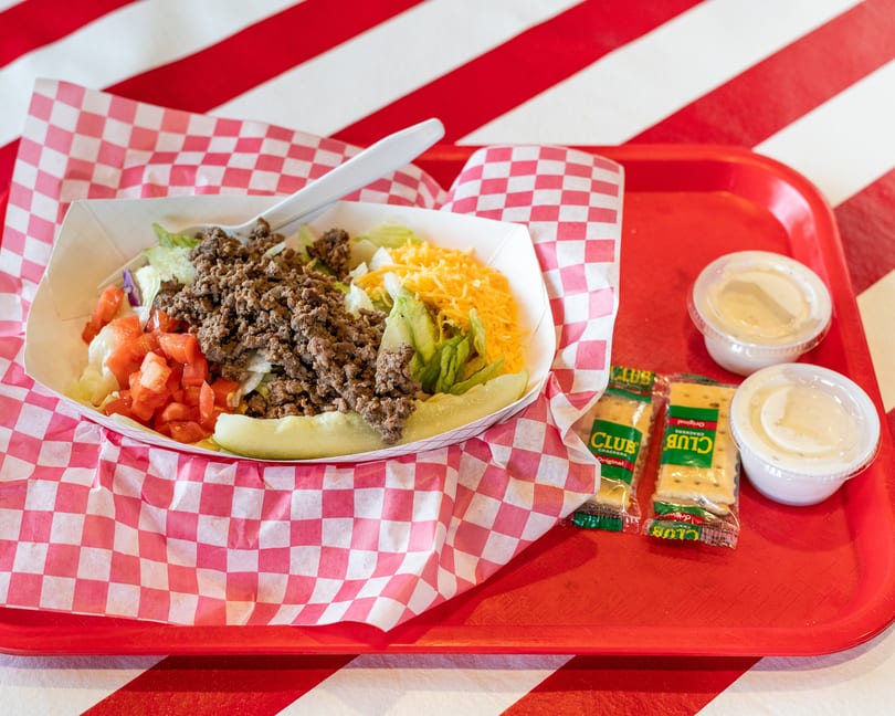 Taco salad with ground beef, lettuce, tomatoes, cheese, and pickles on a red tray.