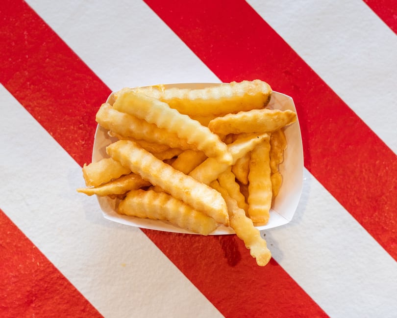 A white paper tray filled with golden, crinkle-cut french fries on a red and white striped surface.
