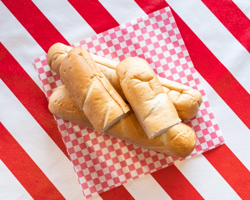 Freshly baked bread rolls on a red and white checkered paper, against a striped background.