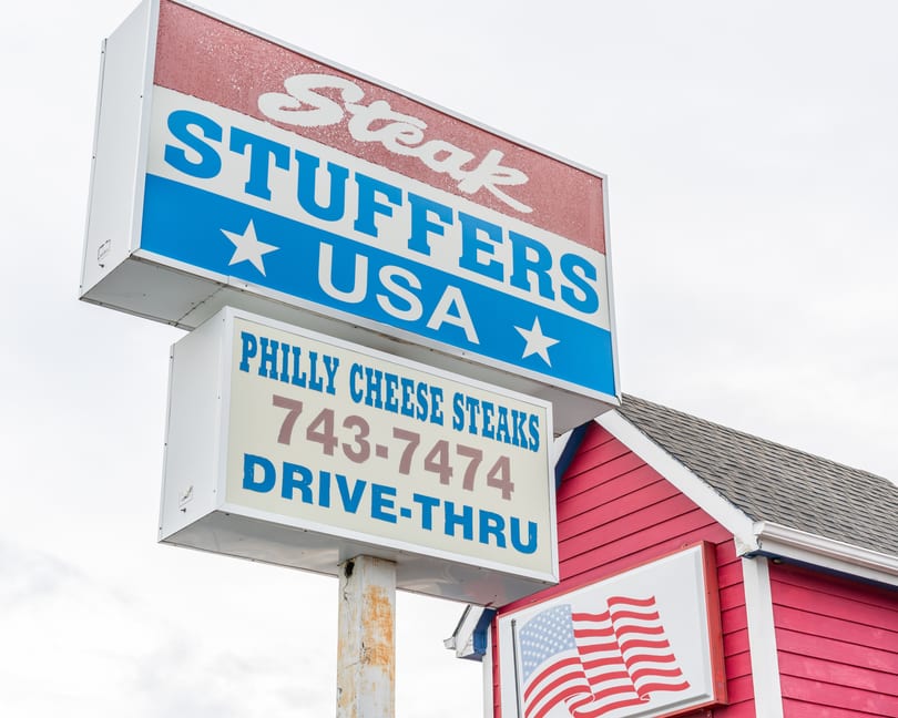 A red and blue sign for "Steak Stuffers USA" advertising "Philly Cheese Steaks" and a drive-thru.