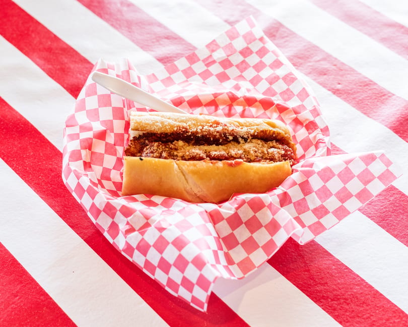 Chicken parmesan hero sandwich with red sauce and grated cheese in a checkered paper basket.