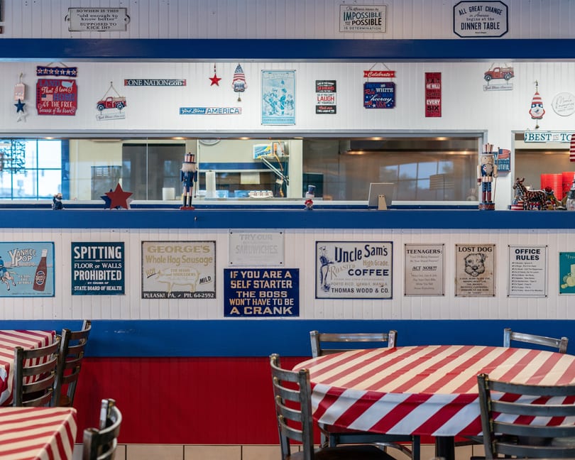 Restaurant interior with red and white striped tablecloths, blue and white walls, and patriotic decor.