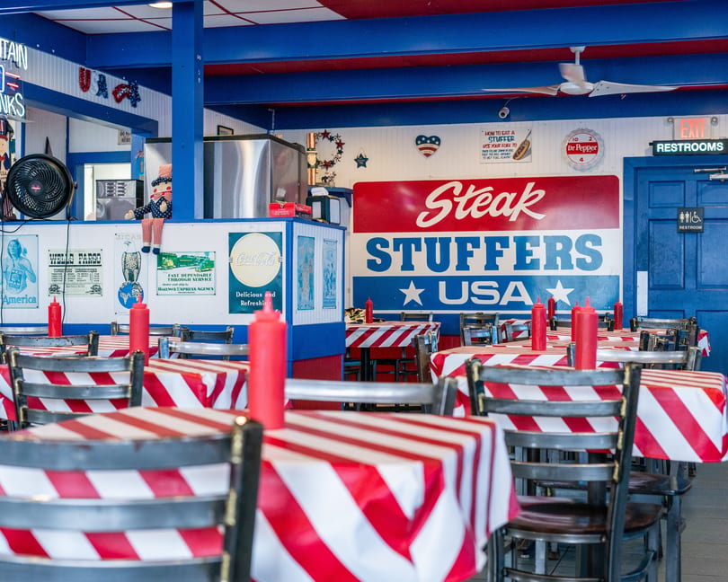 Interior of Steak Stuffers USA, featuring red and white striped tables, blue walls, and patriotic decor.
